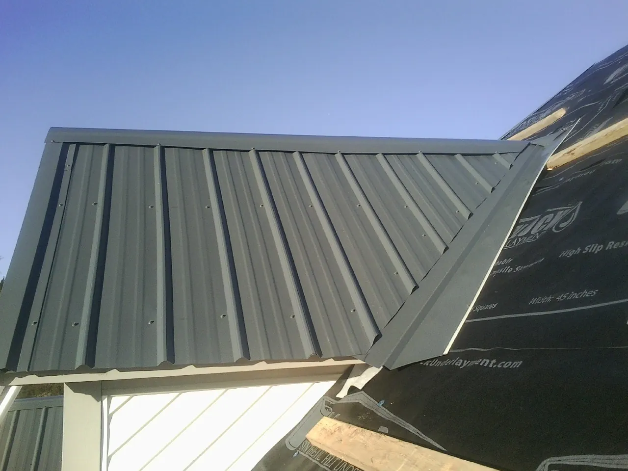 Gray metal roof panels going on over a garage gable in Roscoe