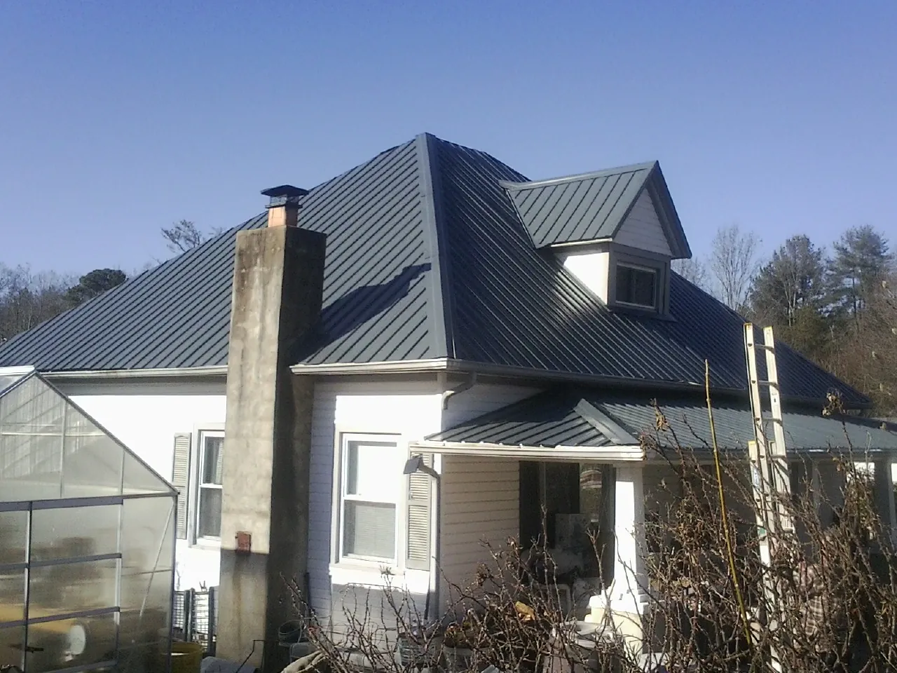 Dark blue standing seam metal roof on a white farmhouse with dormer — Slate & Tile Roof Repair by Roofing Brothers in Roscoe